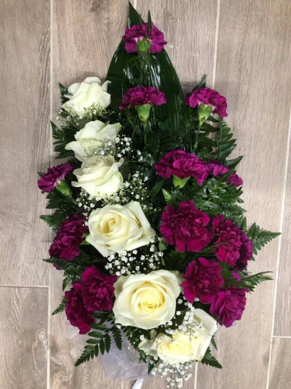 Violeteista ja valkoisista kukista sidottu hautajaiskimppu